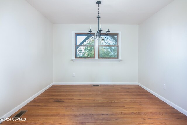 empty room with hardwood / wood-style flooring and a notable chandelier