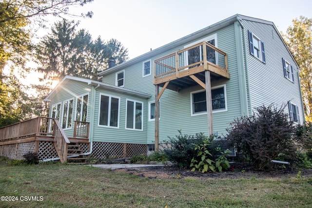 back of property featuring a sunroom, a wooden deck, and a lawn