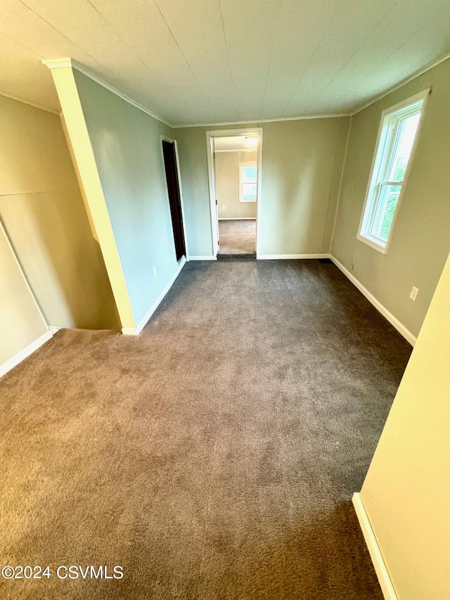 empty room with ornamental molding and dark colored carpet