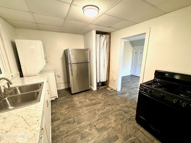 kitchen with black range with gas stovetop, white cabinets, stainless steel refrigerator, a drop ceiling, and sink