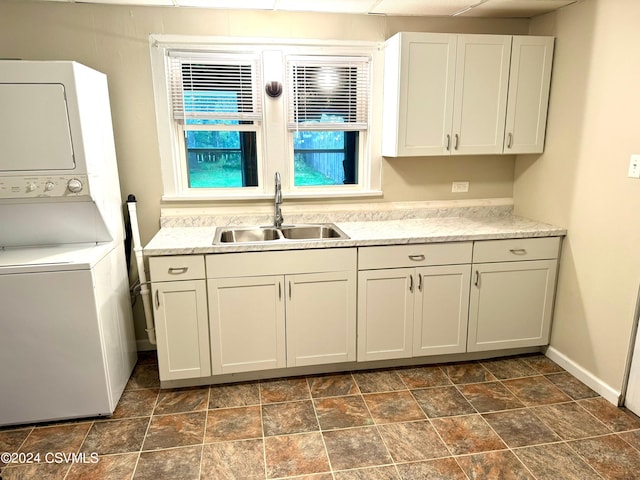 laundry room with cabinets, stacked washer / drying machine, and sink