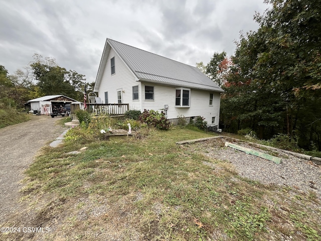 view of side of home featuring metal roof, an outbuilding, a wooden deck, and driveway