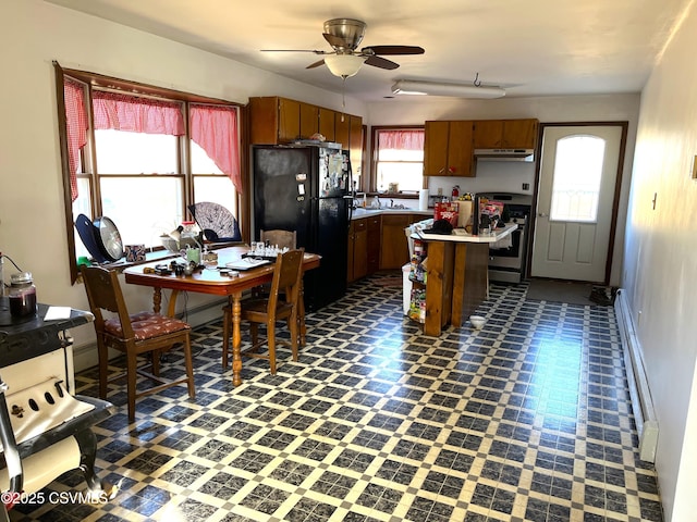 kitchen with dark floors, light countertops, freestanding refrigerator, stainless steel gas range, and under cabinet range hood