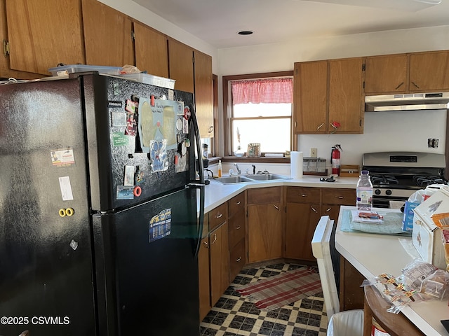 kitchen with under cabinet range hood, a sink, light countertops, freestanding refrigerator, and gas range