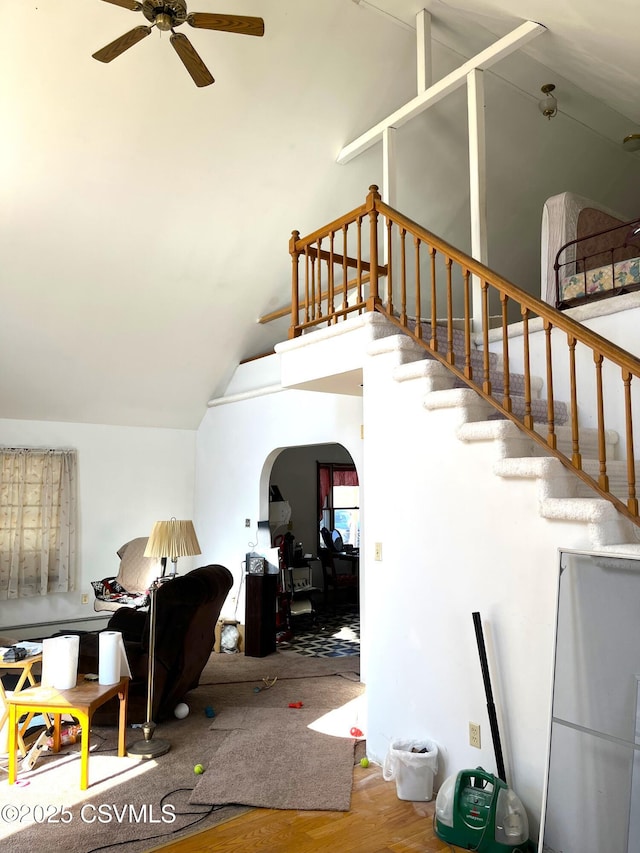 interior space with arched walkways, ceiling fan, stairway, wood finished floors, and high vaulted ceiling