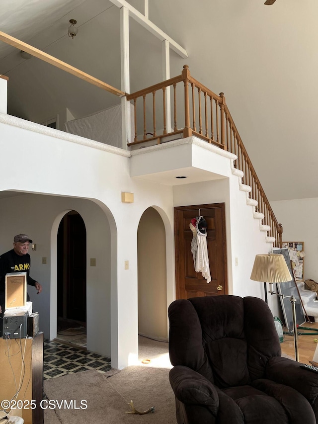 living room featuring arched walkways, a high ceiling, stairway, and carpet