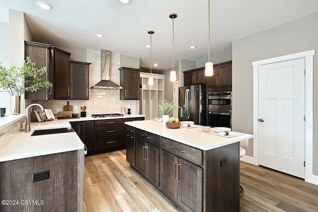 kitchen with pendant lighting, sink, wall chimney exhaust hood, appliances with stainless steel finishes, and a center island