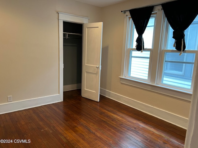 unfurnished bedroom with a closet, dark wood-type flooring, and multiple windows