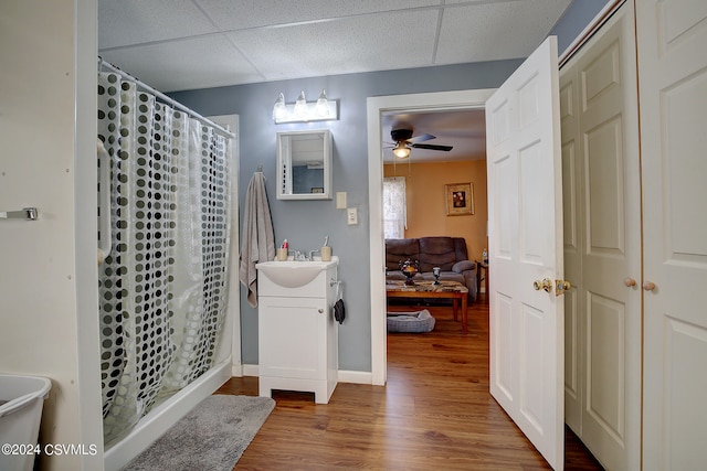 bathroom with vanity, walk in shower, wood-type flooring, ceiling fan, and a paneled ceiling