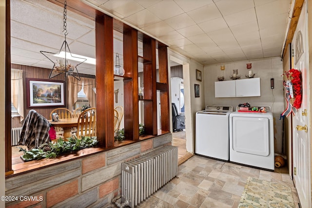 laundry area featuring separate washer and dryer, radiator heating unit, an inviting chandelier, cabinets, and wooden walls