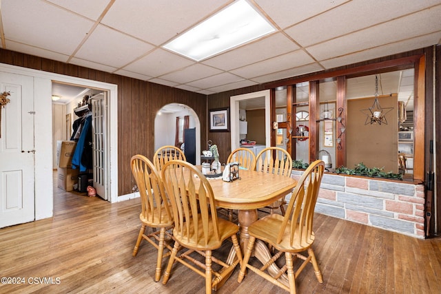 dining room featuring hardwood / wood-style flooring, a drop ceiling, and wood walls