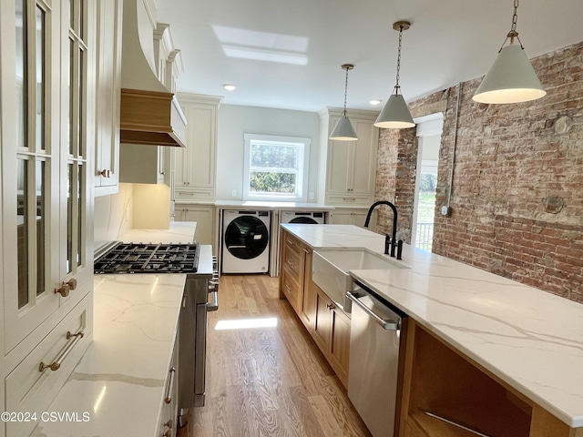 kitchen with stainless steel appliances, washer / clothes dryer, brick wall, and light stone counters