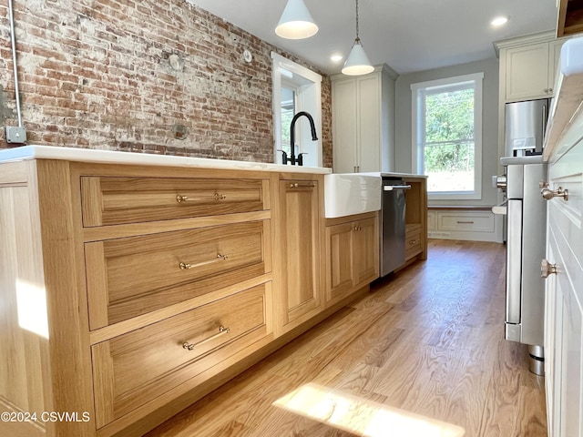 kitchen with sink, light hardwood / wood-style flooring, stainless steel appliances, decorative light fixtures, and brick wall