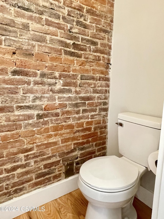 bathroom with brick wall, hardwood / wood-style floors, and toilet