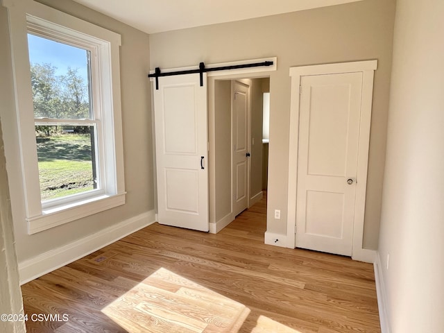 unfurnished bedroom with a closet, light hardwood / wood-style flooring, a barn door, and multiple windows