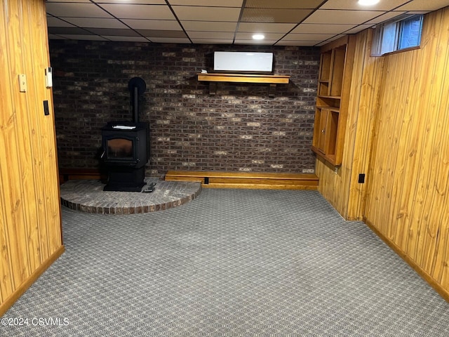 basement with a paneled ceiling, brick wall, carpet floors, and wooden walls