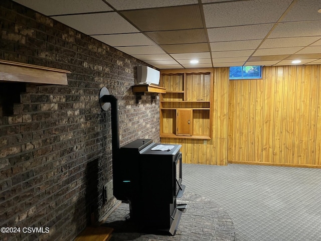 carpeted home office with an AC wall unit, a drop ceiling, wooden walls, and brick wall