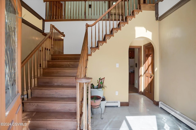 staircase featuring tile patterned floors, arched walkways, a towering ceiling, and a baseboard heating unit
