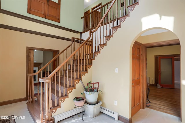 stairs with a baseboard radiator, arched walkways, a baseboard heating unit, and a high ceiling