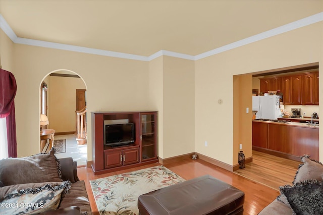 living room featuring ornamental molding, light wood-style flooring, arched walkways, and baseboards