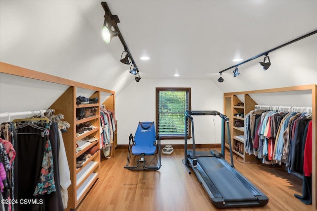 workout area with light wood-style floors, baseboards, rail lighting, and vaulted ceiling