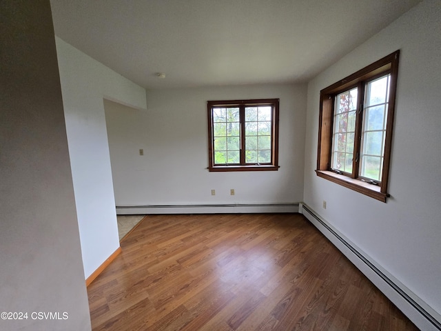 unfurnished room with baseboards, a baseboard radiator, wood finished floors, and a healthy amount of sunlight