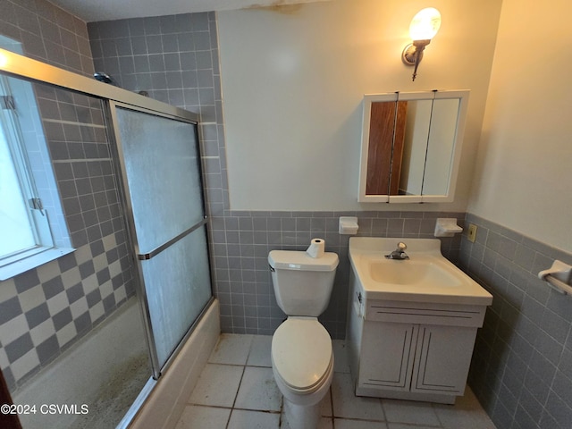 full bathroom with shower / bath combination with glass door, toilet, tile patterned floors, tile walls, and vanity