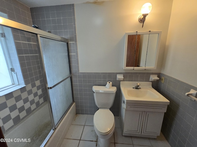 bathroom with tile patterned flooring, bath / shower combo with glass door, vanity, and tile walls