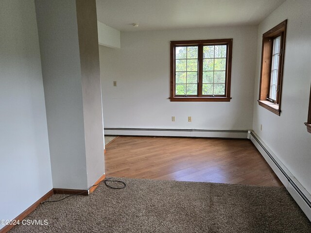 empty room featuring baseboards, a baseboard heating unit, and wood finished floors