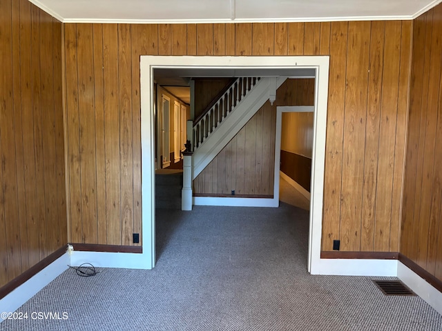 empty room with ornamental molding, wood walls, and dark colored carpet