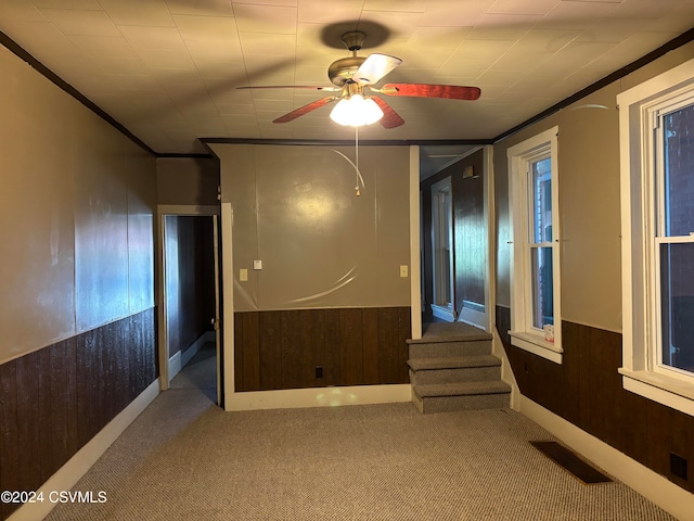 carpeted empty room featuring ceiling fan, wood walls, and crown molding