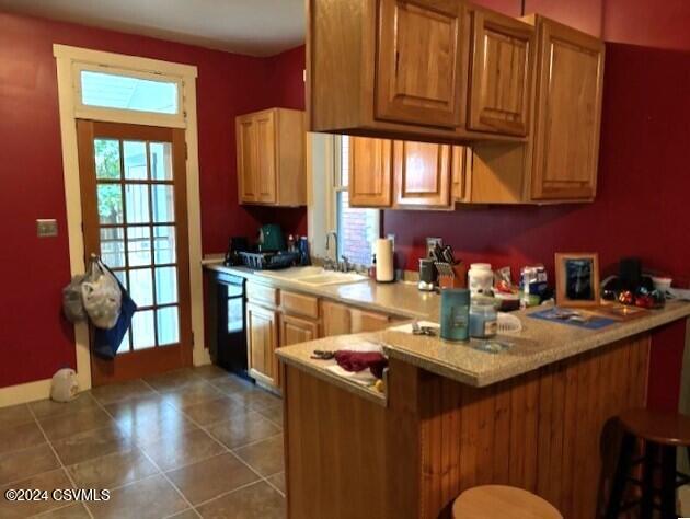 kitchen featuring dark tile patterned flooring, sink, kitchen peninsula, a breakfast bar area, and black dishwasher