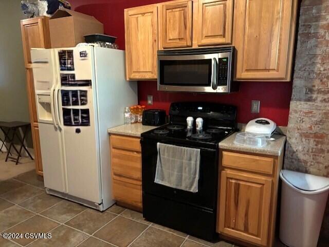 kitchen featuring black range with electric stovetop, white refrigerator with ice dispenser, and dark tile patterned flooring