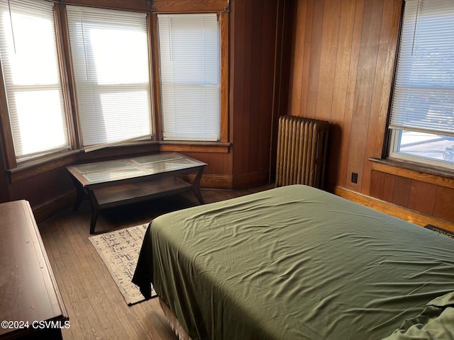 bedroom featuring radiator, hardwood / wood-style flooring, wooden walls, and multiple windows