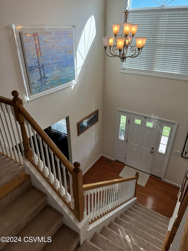 foyer entrance with wood-type flooring, a high ceiling, a notable chandelier, and a wealth of natural light