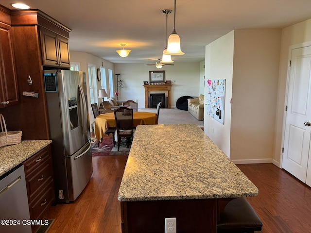 kitchen with light stone counters, pendant lighting, dark wood-type flooring, stainless steel appliances, and a center island