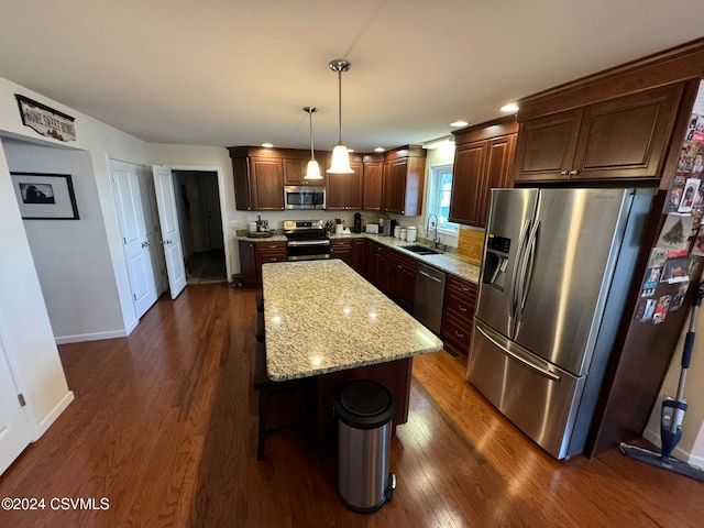 kitchen with a kitchen island, dark hardwood / wood-style flooring, light stone counters, stainless steel appliances, and hanging light fixtures