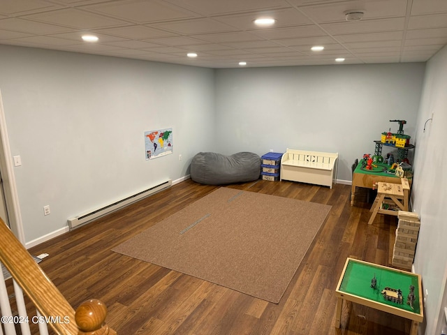 recreation room with baseboard heating, a drop ceiling, and dark hardwood / wood-style flooring