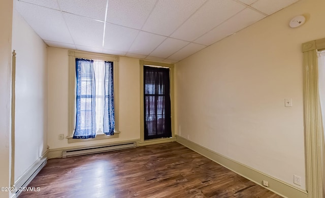 spare room with baseboard heating, dark wood-type flooring, and a drop ceiling