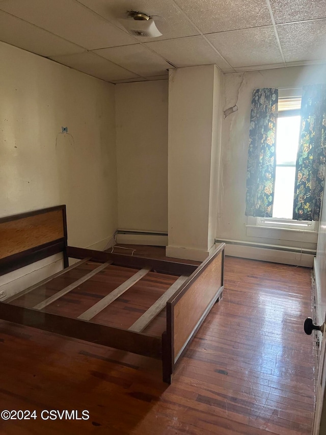 unfurnished bedroom featuring a drop ceiling, dark hardwood / wood-style floors, and a baseboard heating unit