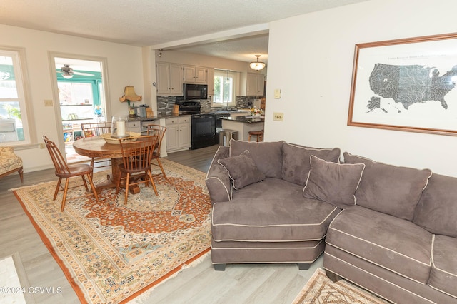 living room with light hardwood / wood-style floors, a textured ceiling, and ceiling fan