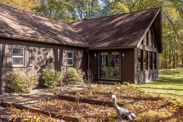 view of front facade featuring a shingled roof, a vegetable garden, a front lawn, and french doors