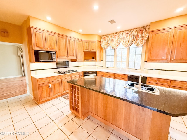 kitchen with black appliances, light tile patterned floors, sink, dark stone countertops, and a center island