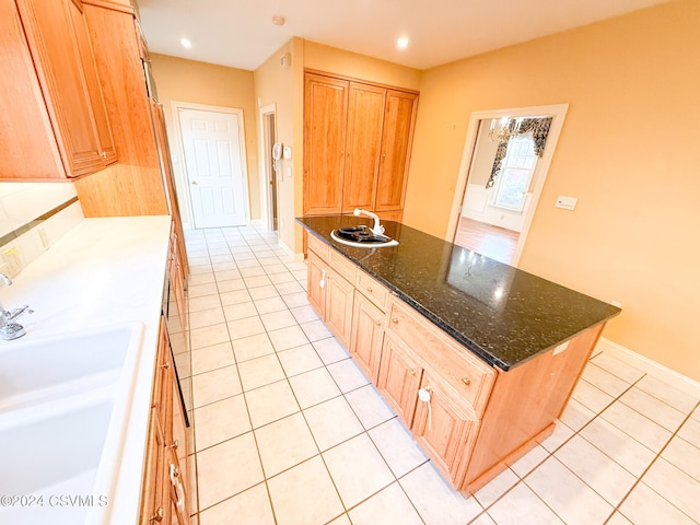 kitchen with an island with sink, light tile patterned flooring, dark stone counters, and sink