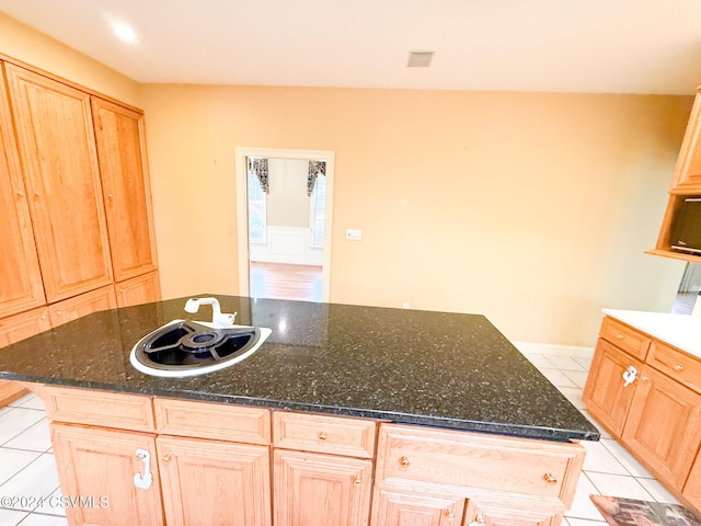 kitchen featuring sink, light brown cabinetry, dark stone countertops, light tile patterned floors, and an island with sink