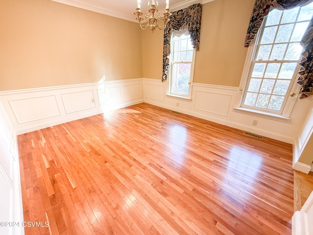 empty room featuring light wood-type flooring, a chandelier, and crown molding