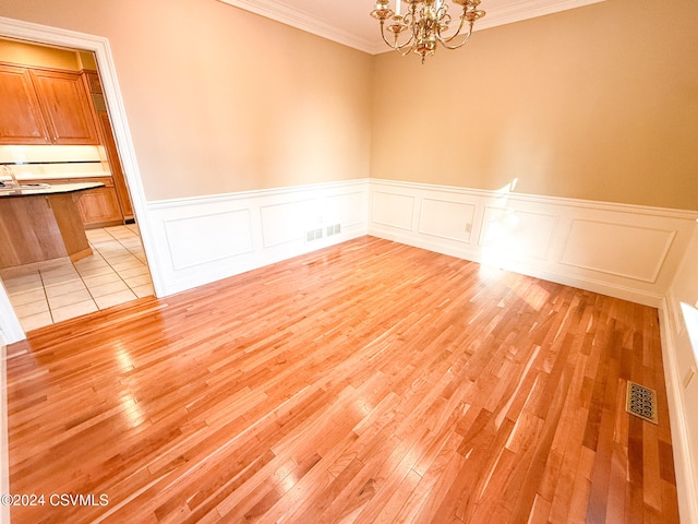 unfurnished room featuring light hardwood / wood-style flooring, sink, crown molding, and an inviting chandelier