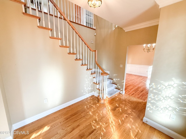 stairs featuring hardwood / wood-style floors, an inviting chandelier, and crown molding