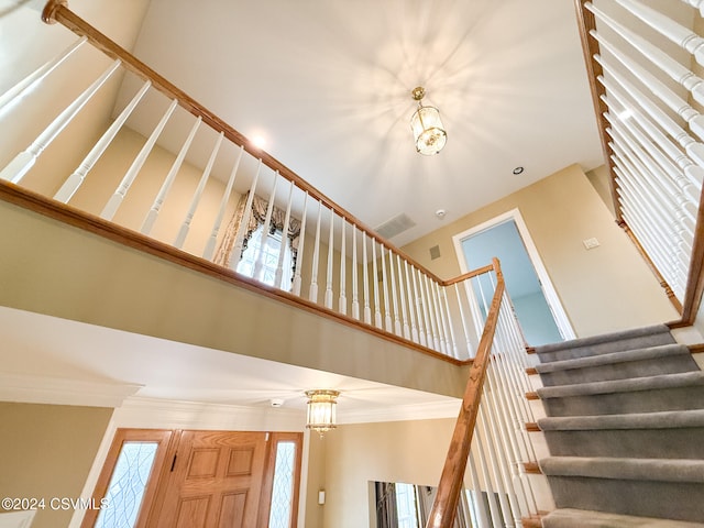 stairs with ornamental molding, a notable chandelier, and a high ceiling