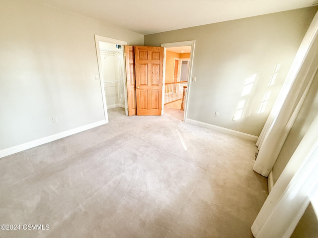 unfurnished bedroom featuring a closet, a walk in closet, and light carpet